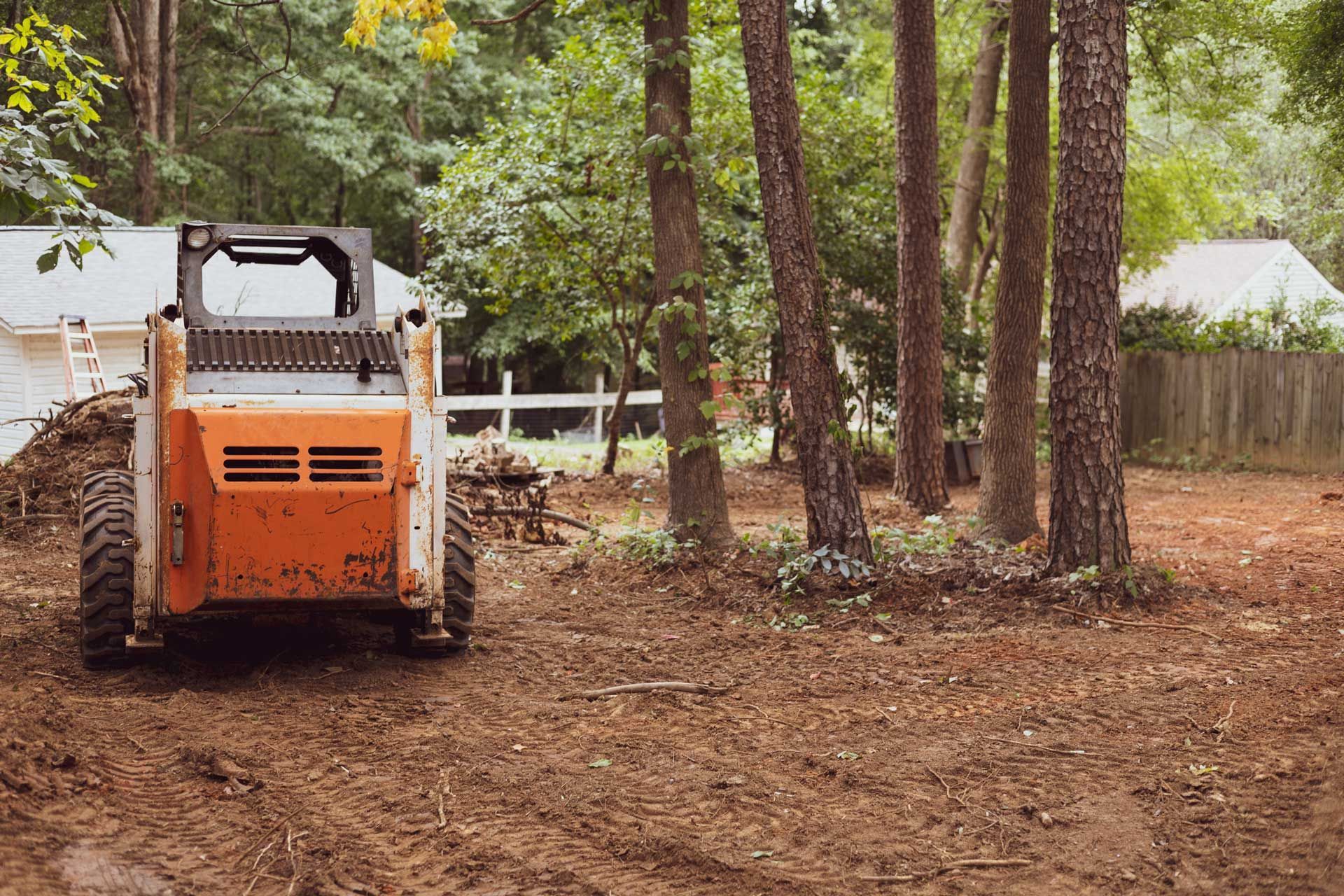 A skid steer is parked in a dirt lot in front of a house.