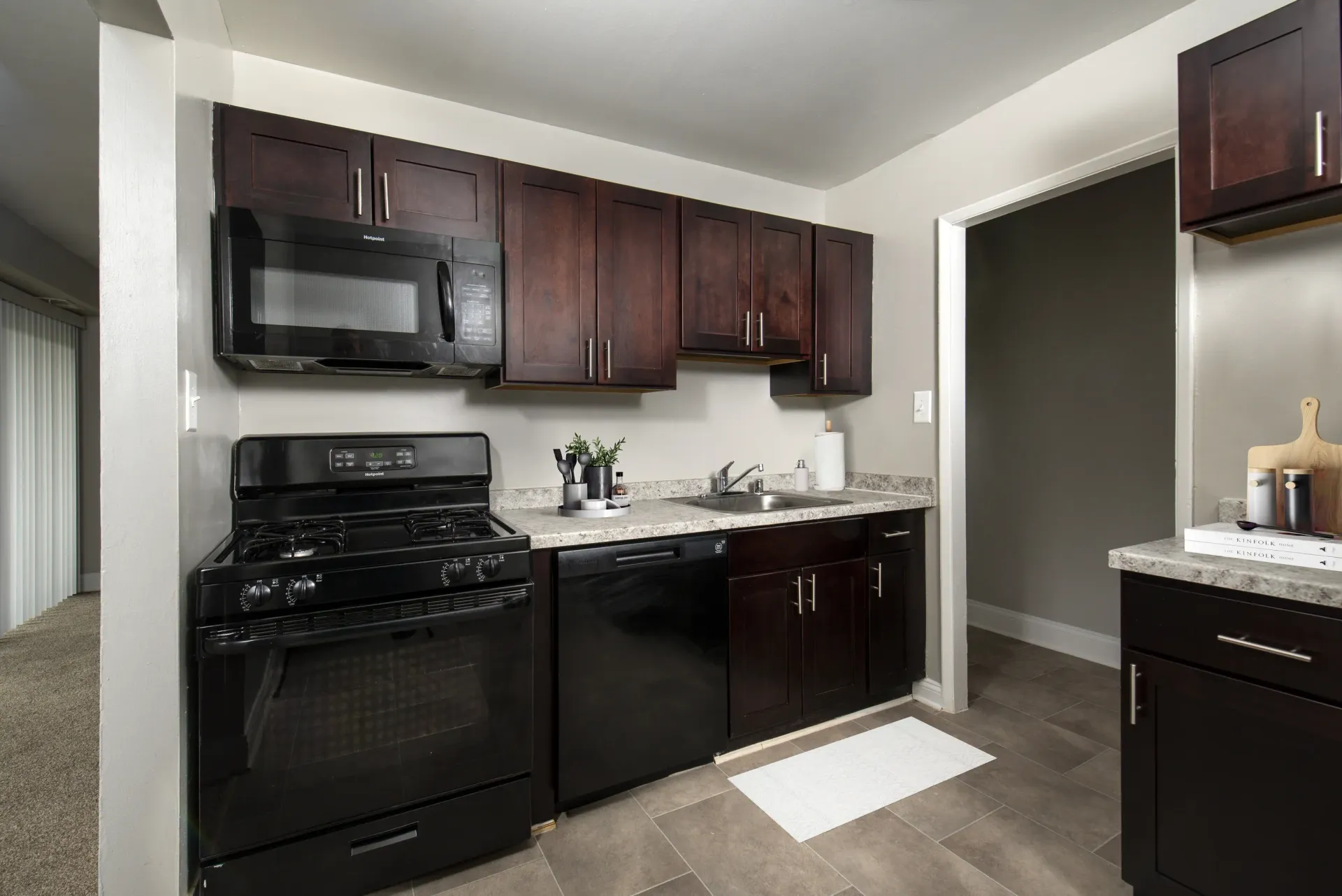 Apartment kitchen with dark wood cabinets, black stove and microwave, and a sink at Metro Pointe in Baltimore, MD.