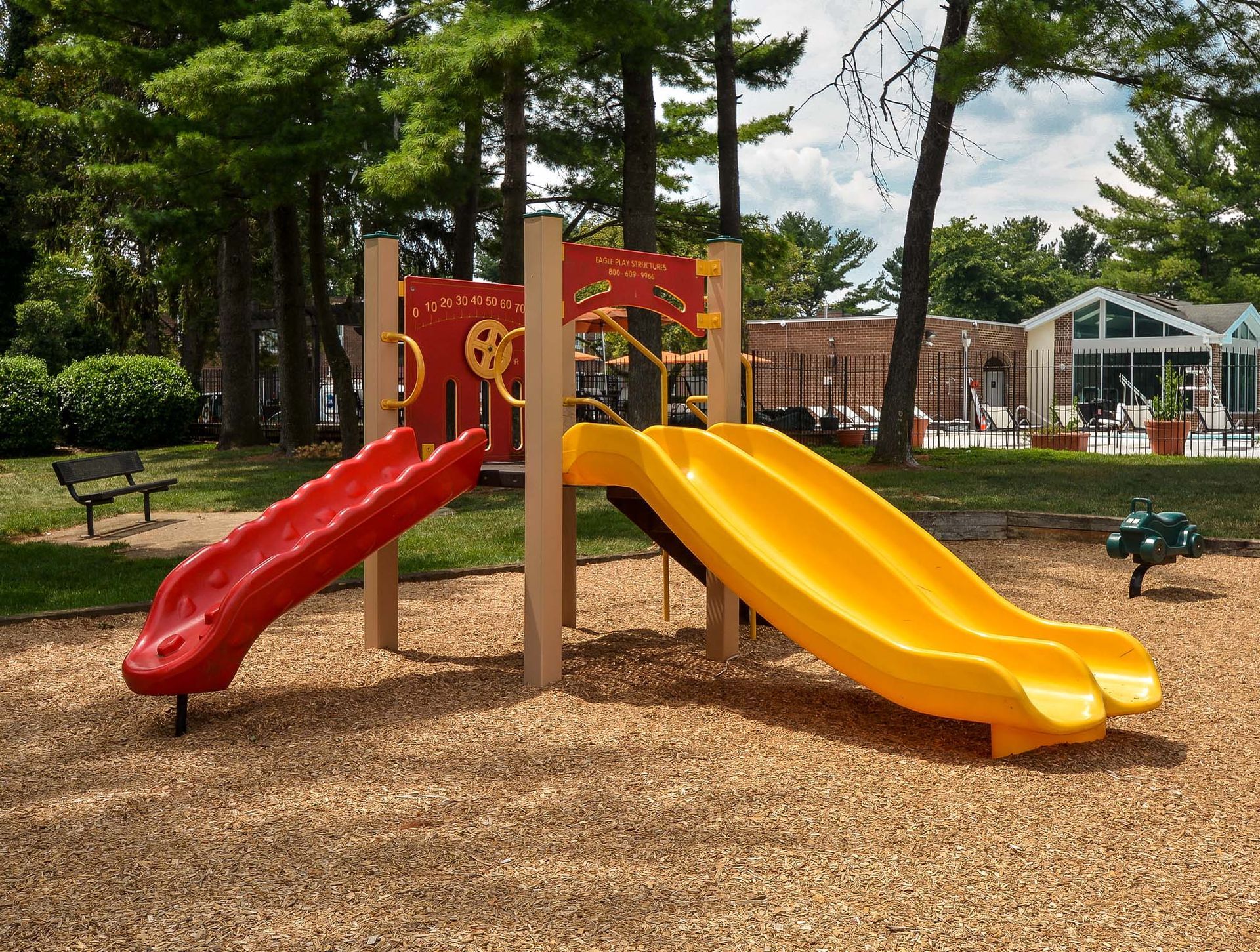 Playground with red and yellow slides in a tree-lined courtyard at Metro Pointe in Baltimore, MD.