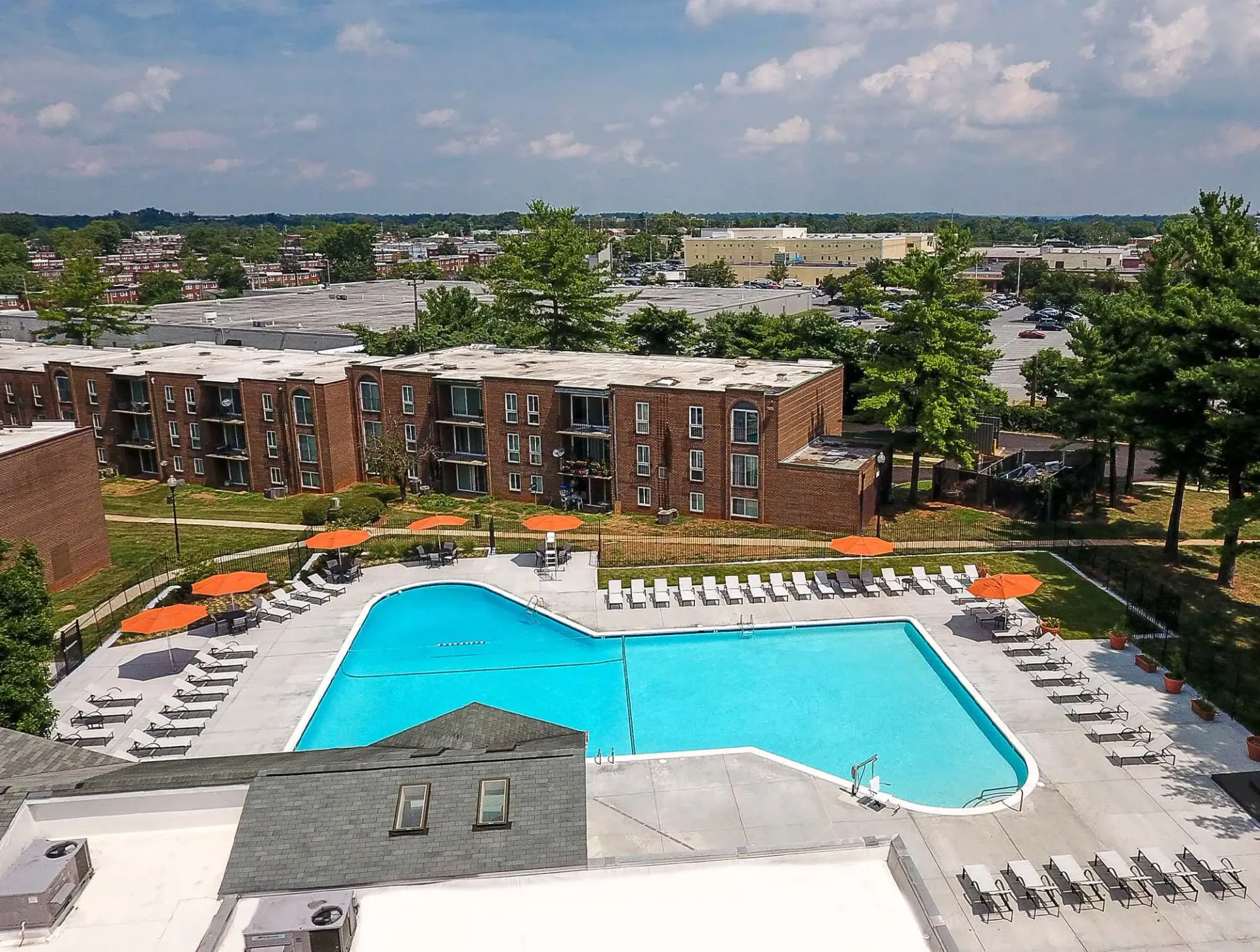 Aerial view of a brick apartment complex with a large pool and orange umbrellas at Metro Pointe in Baltimore, MD.