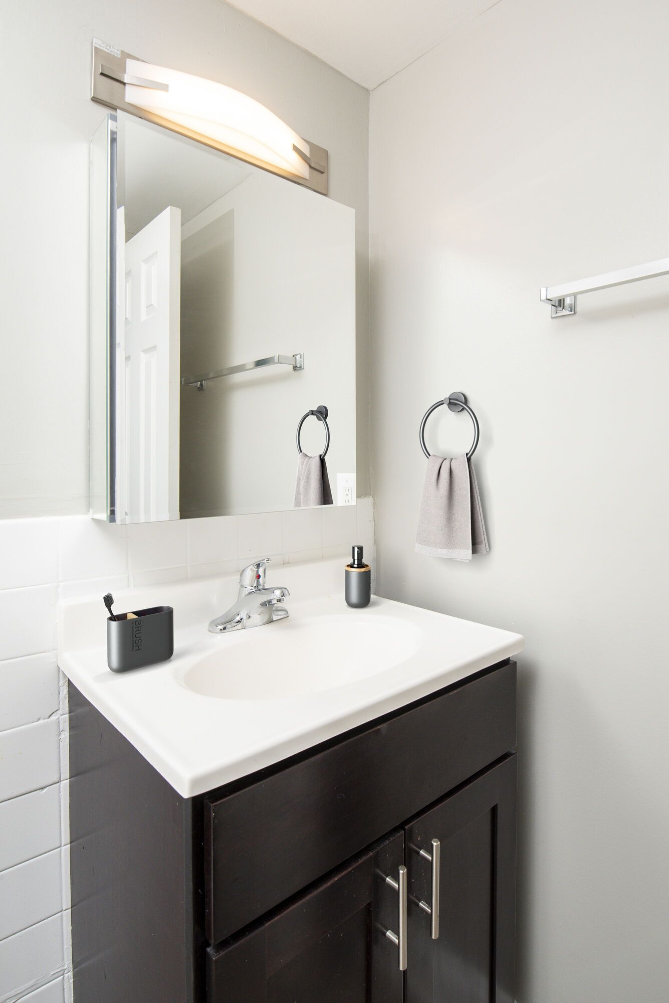Bathroom vanity with white sink, dark wood cabinet, and wall mirror with towel rings at Metro Pointe in Baltimore, MD.