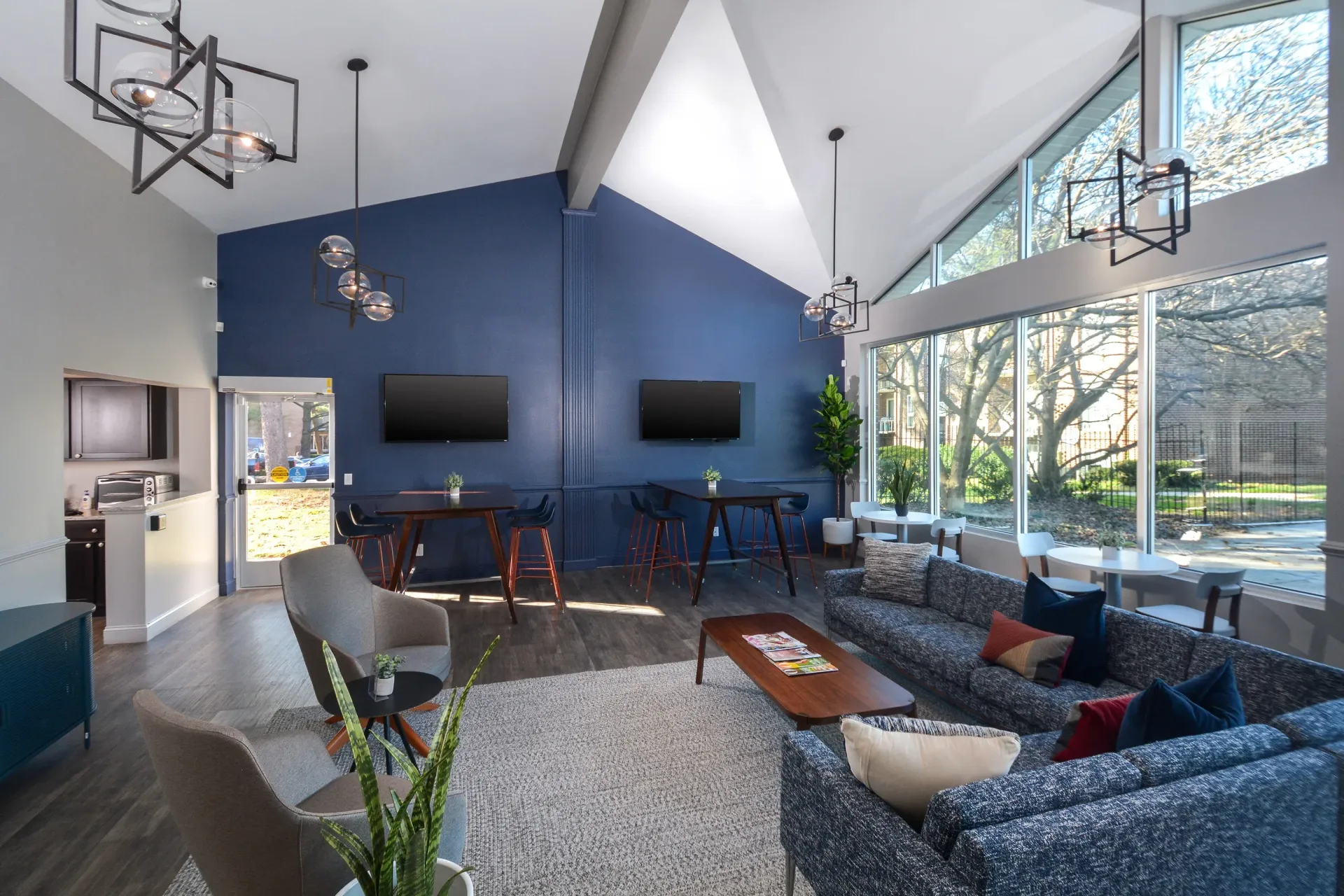 Bright modern community lounge with blue accent wall, sofas, small tables, and wall-mounted TVs at Metro Pointe in Baltimore, MD.