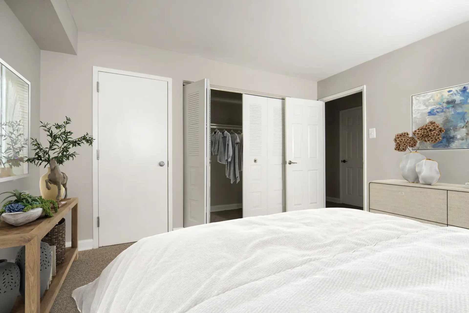 Bedroom in an apartment with a bed, dresser, and an open closet showing hanging clothes at Metro Pointe in Baltimore, MD.