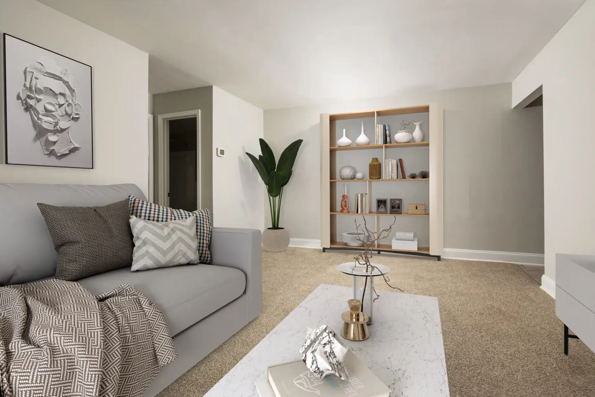 Living room in a modern apartment with a gray sofa, beige carpet, and a tall bookshelf at Metro Pointe in Baltimore, MD.
