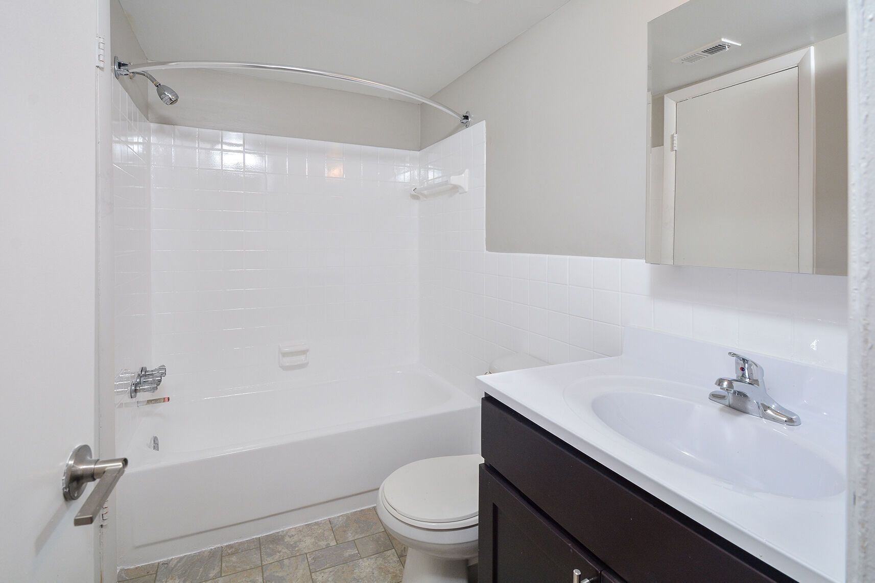 White-tiled apartment bathroom with a bathtub, curved shower rod, toilet, and dark vanity at Metro Pointe in Baltimore, MD.