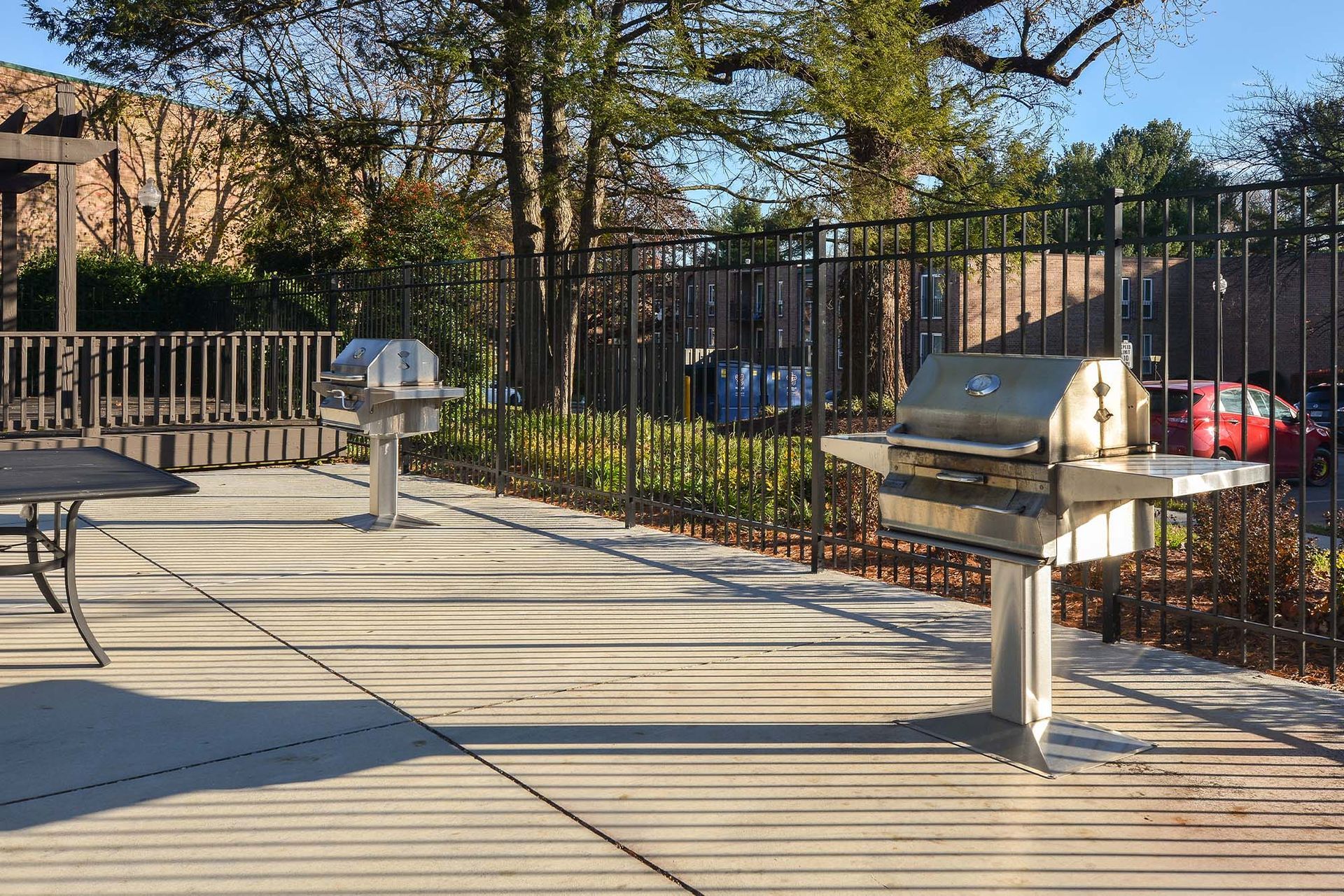 Outdoor communal grilling area with two stainless steel grills on a concrete patio, fenced and tree-shaded at Metro Pointe in Baltimore, MD.