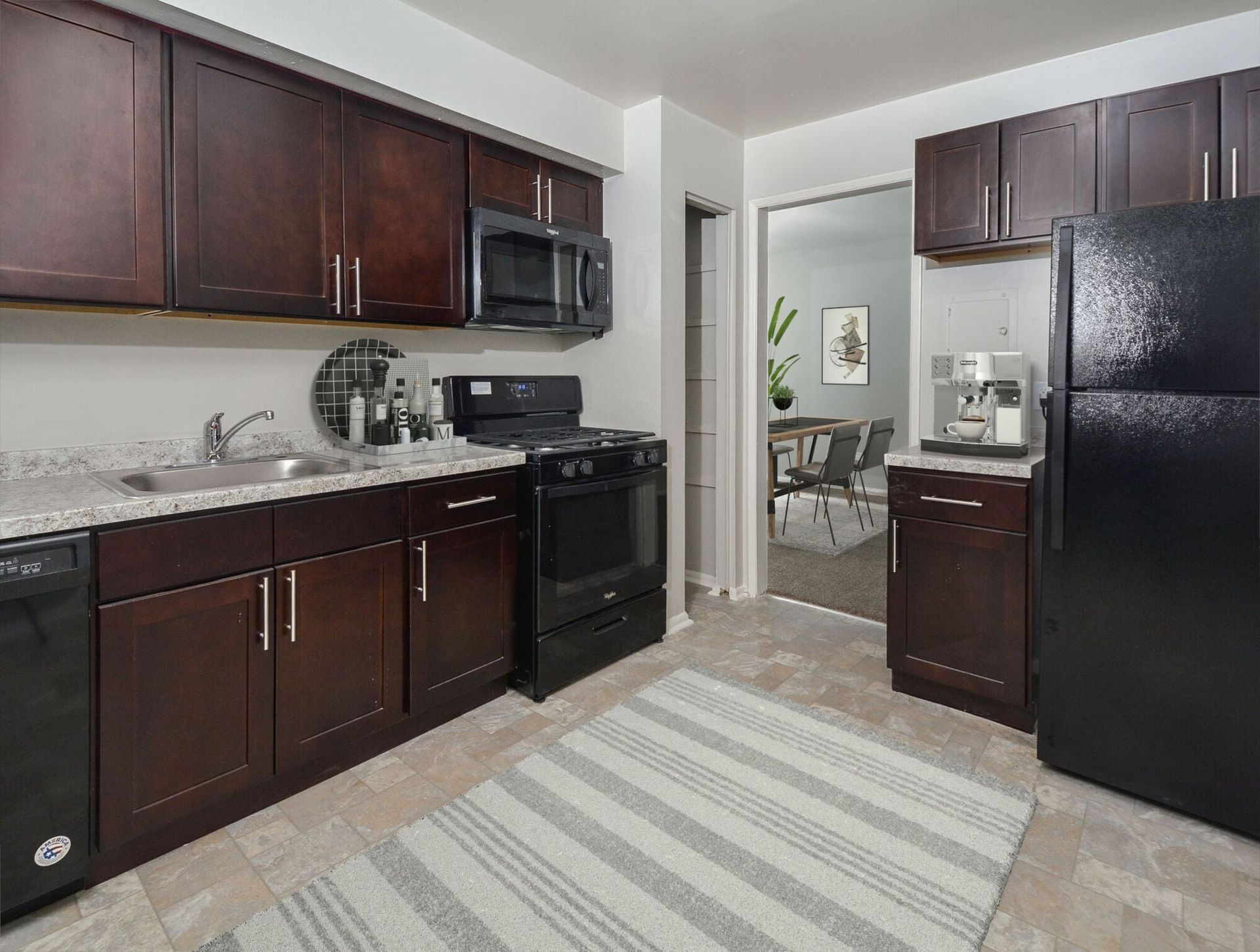 Kitchen with dark wood cabinets, black appliances, and a doorway to a dining area at Metro Pointe in Baltimore, MD.
