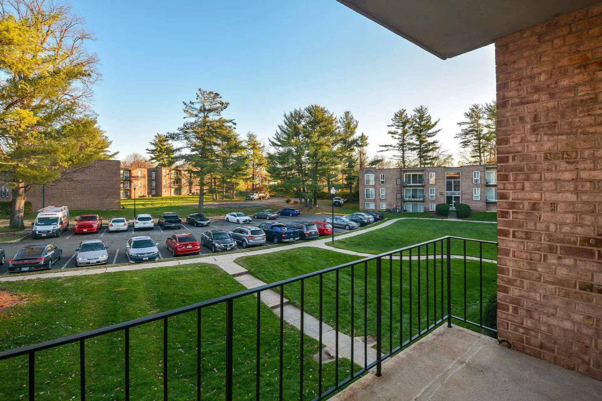 Balcony view overlooking a parking lot, green lawn, and brick apartment buildings at Metro Pointe in Baltimore, MD.