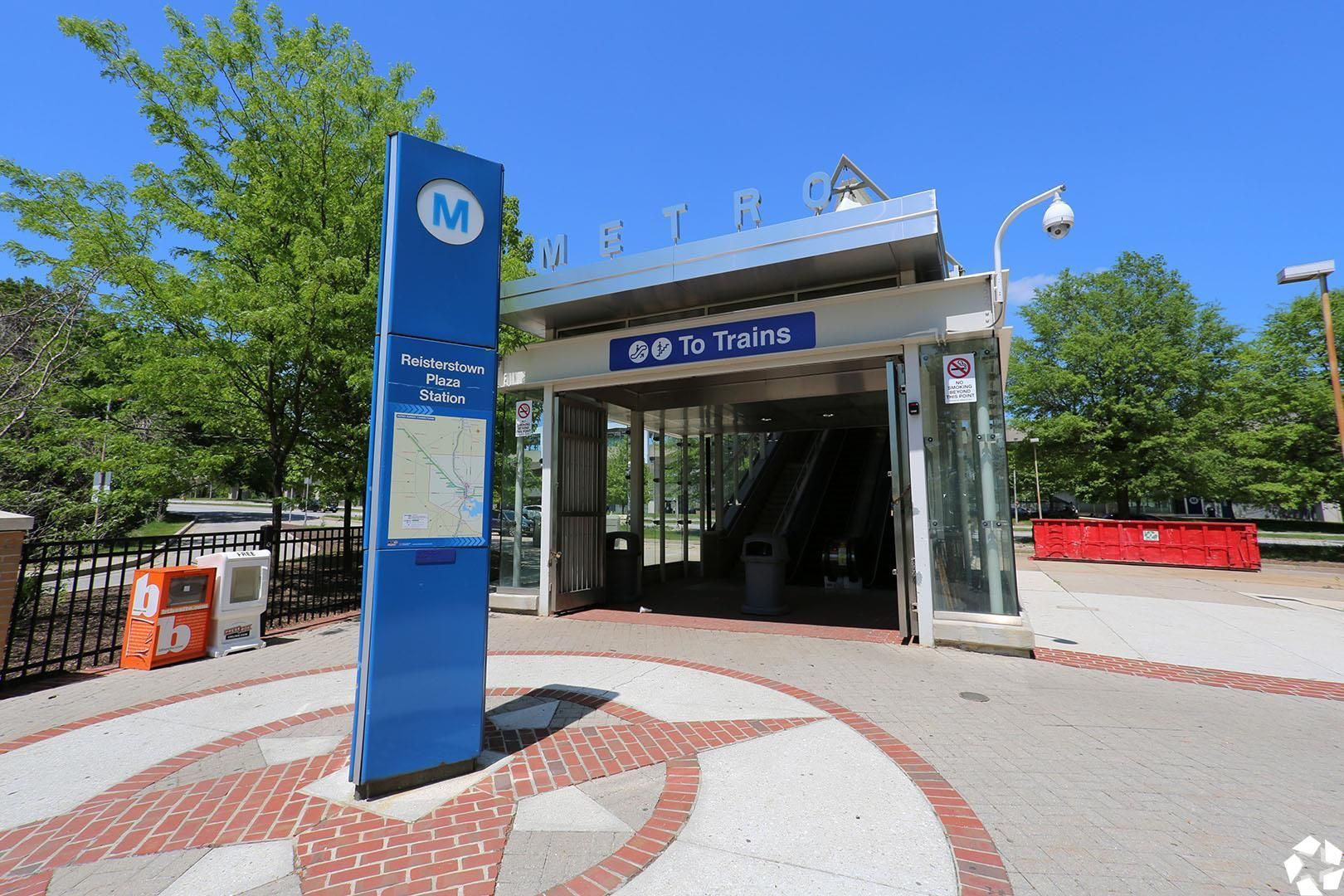 Metro entrance with blue pillar and 'To Trains' sign at Reisterstown Plaza Station on a sunny day at Metro Pointe in Baltimore, MD.