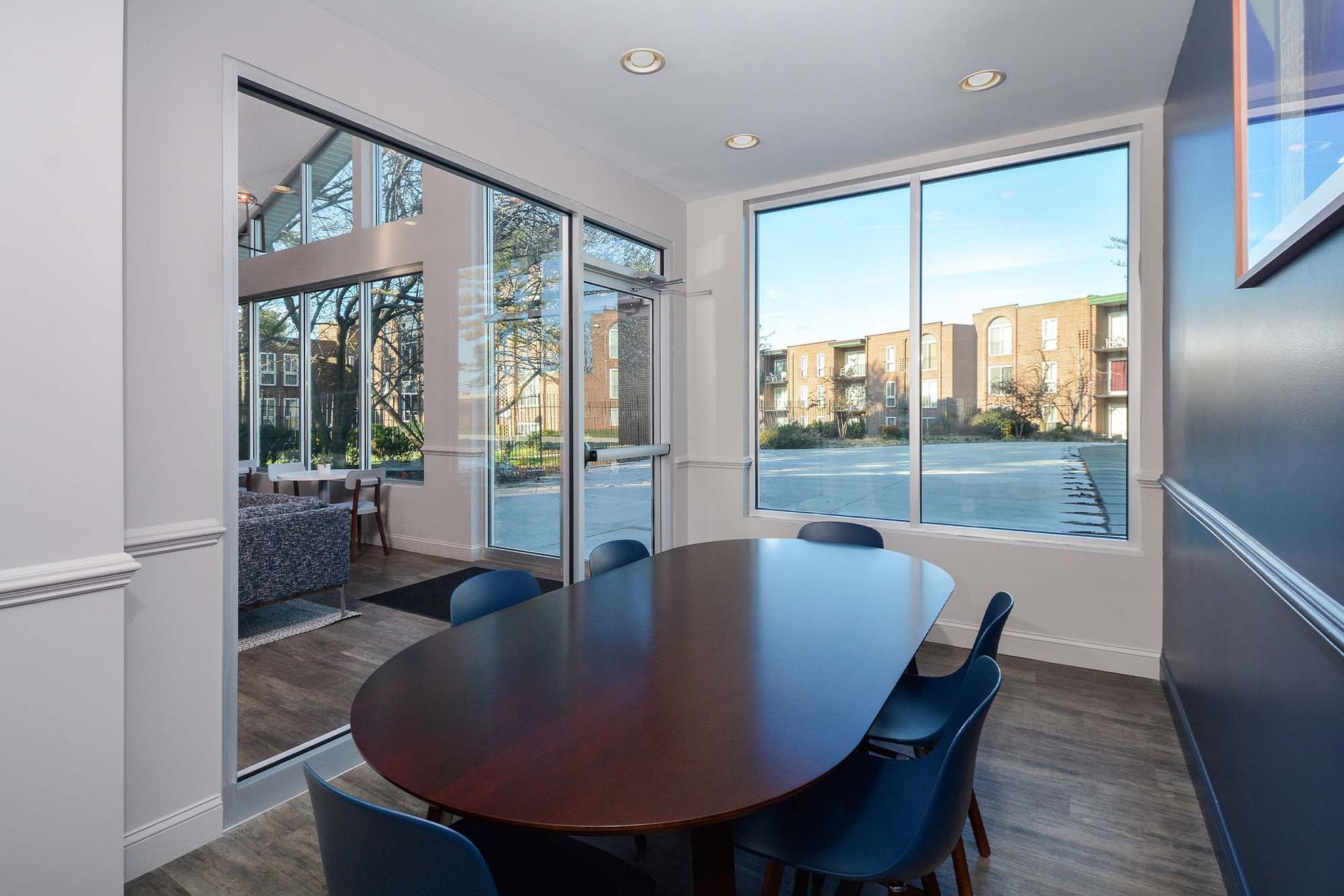 Interior of a community meeting room with a large oval table and blue chairs near glass walls at Metro Pointe in Baltimore, MD.