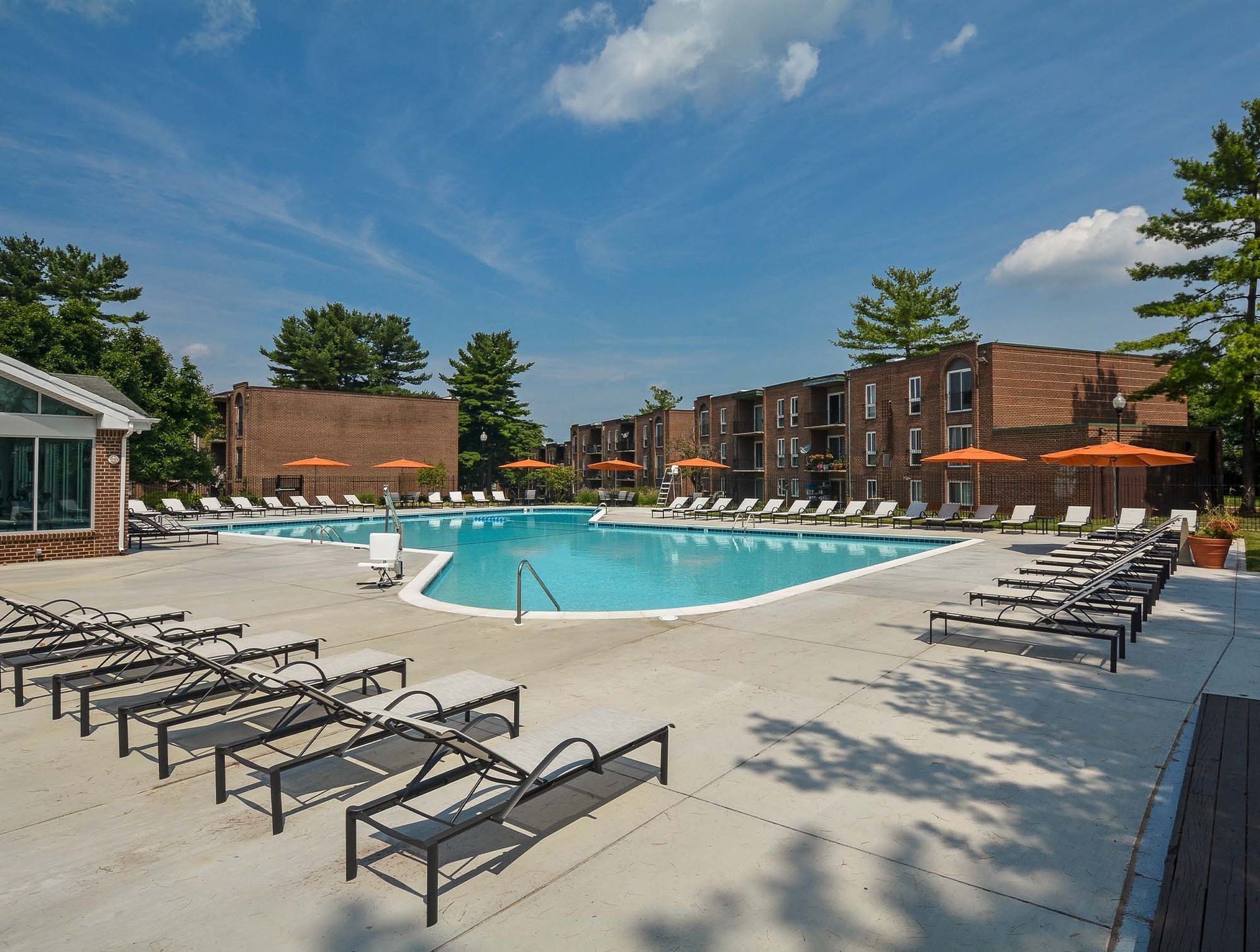 Outdoor community pool with lounge chairs, orange umbrellas, and brick apartment buildings at Metro Pointe in Baltimore, MD.