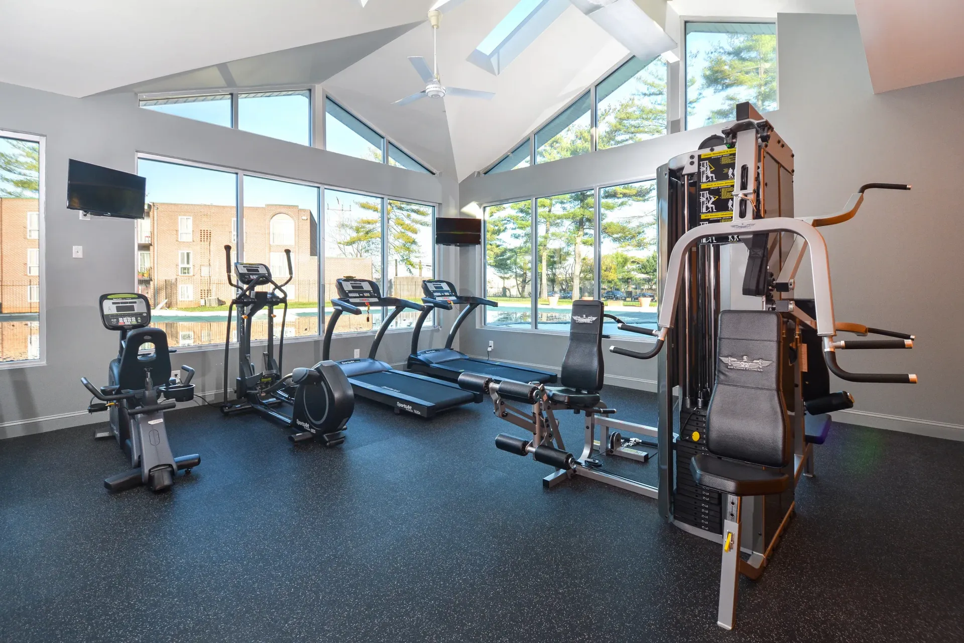 On-site fitness center with cardio machines and weight equipment by large windows at Metro Pointe in Baltimore, MD.