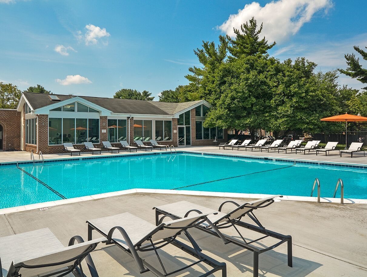 Outdoor community pool with lounge chairs and a brick clubhouse in a sunny setting at Metro Pointe in Baltimore, MD.