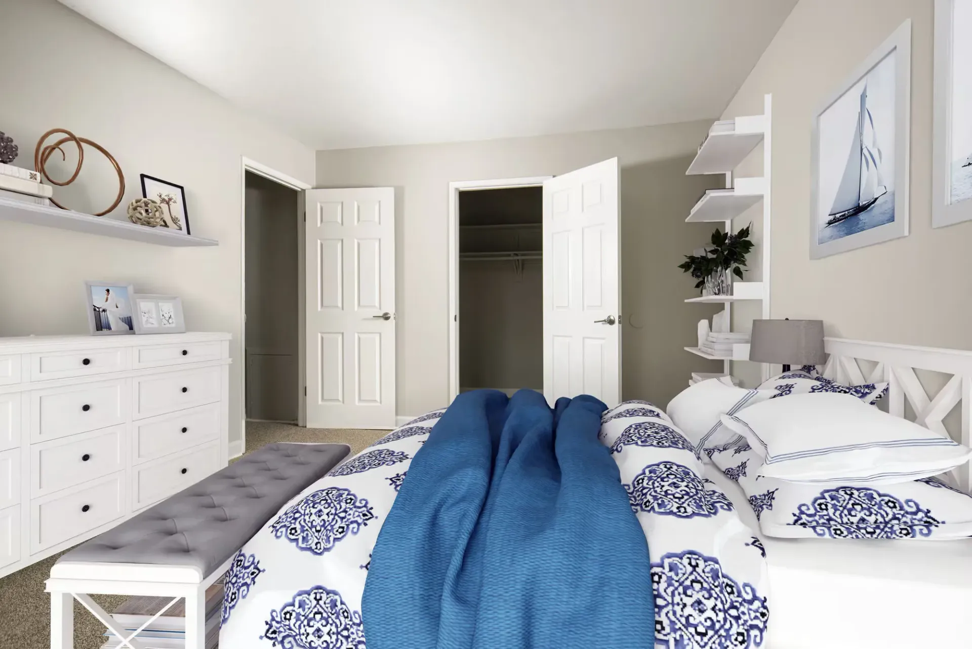 Bedroom with white furniture, blue bedding, bench at foot, and open closet doors at Metro Pointe in Baltimore, MD.