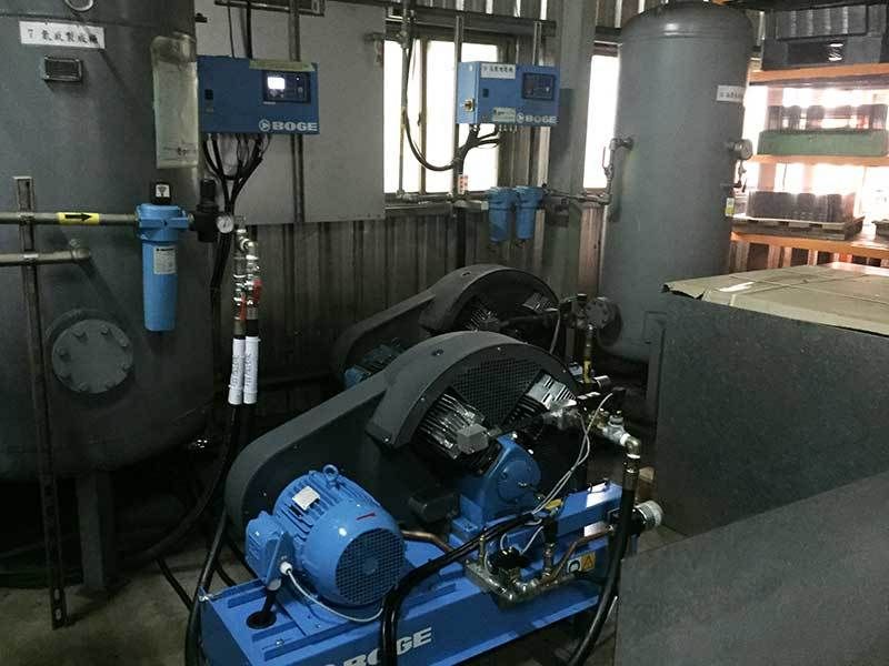 A blue air compressor is sitting in a room next to a tank.