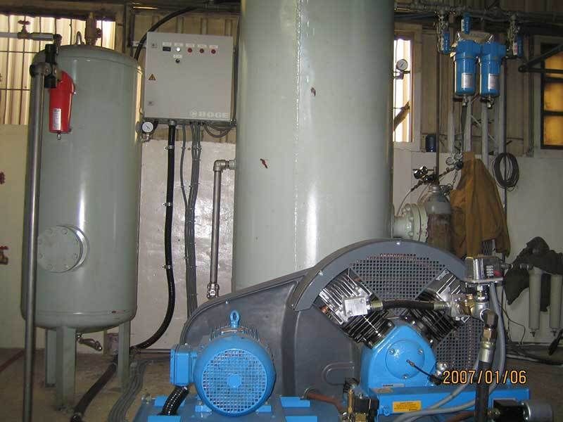 A blue air compressor is sitting in a room next to a tank.