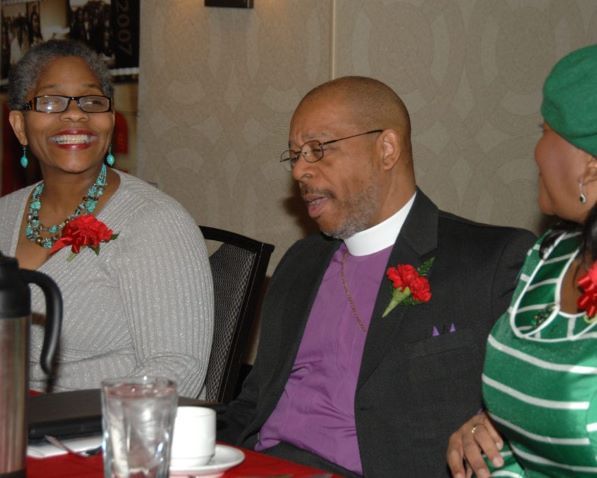A man in a purple suit sits at a table with two women