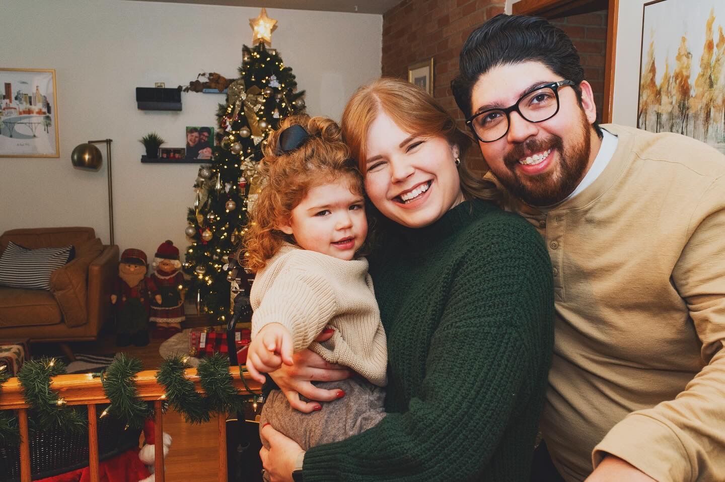 A man and woman are holding a little girl in front of a christmas tree.