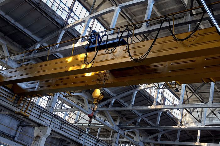 Industrial overhead crane with yellow metal beam and lifting hook in a large warehouse. Steel structure with cables and pulleys for heavy load handling in manufacturing, construction, logistics