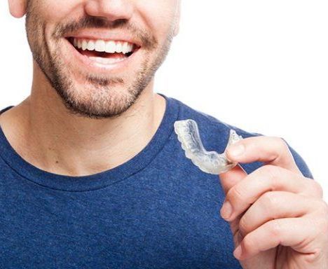 A man is smiling while holding a clear retainer in his hand.