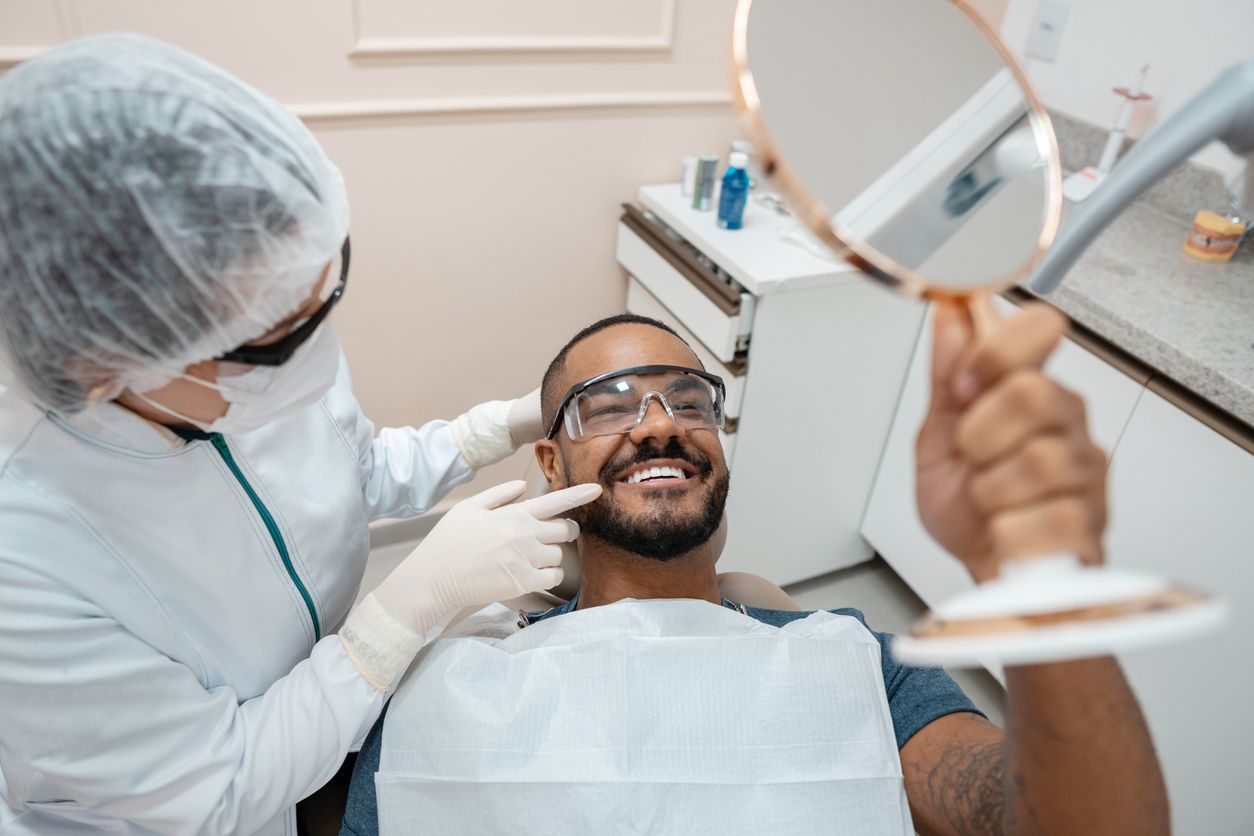 A man is sitting in a dental chair while a dentist examines his teeth.