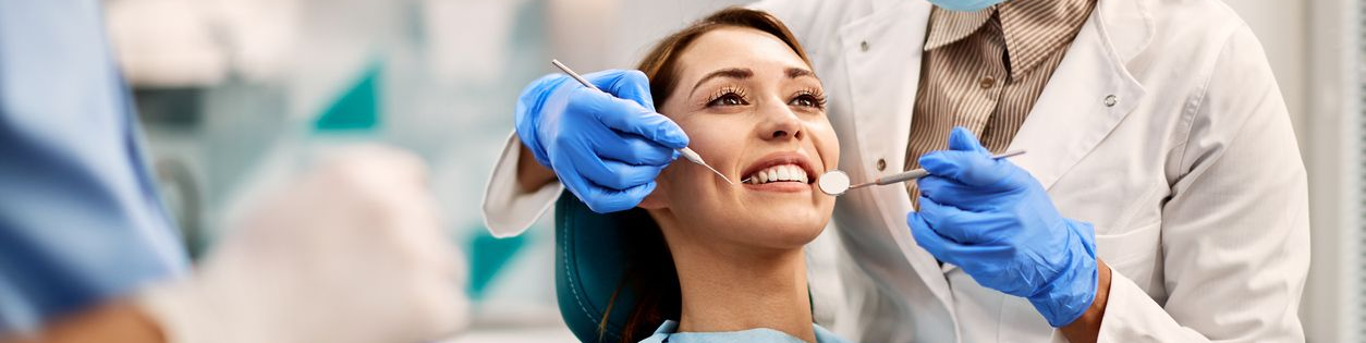 Woman smiles in a dentist's chair. She has dark hair and a red top. The setting appears to be a dental office.