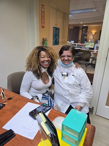 Two women are posing for a picture in an office while sitting at a desk.
