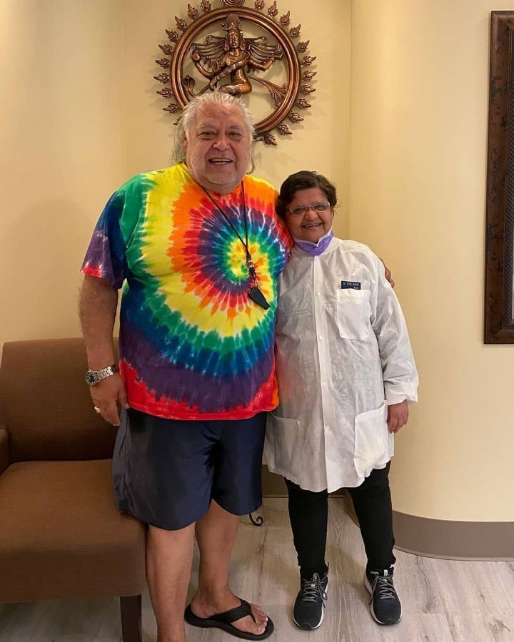 A man in a tie dye shirt is standing next to a woman in a lab coat.