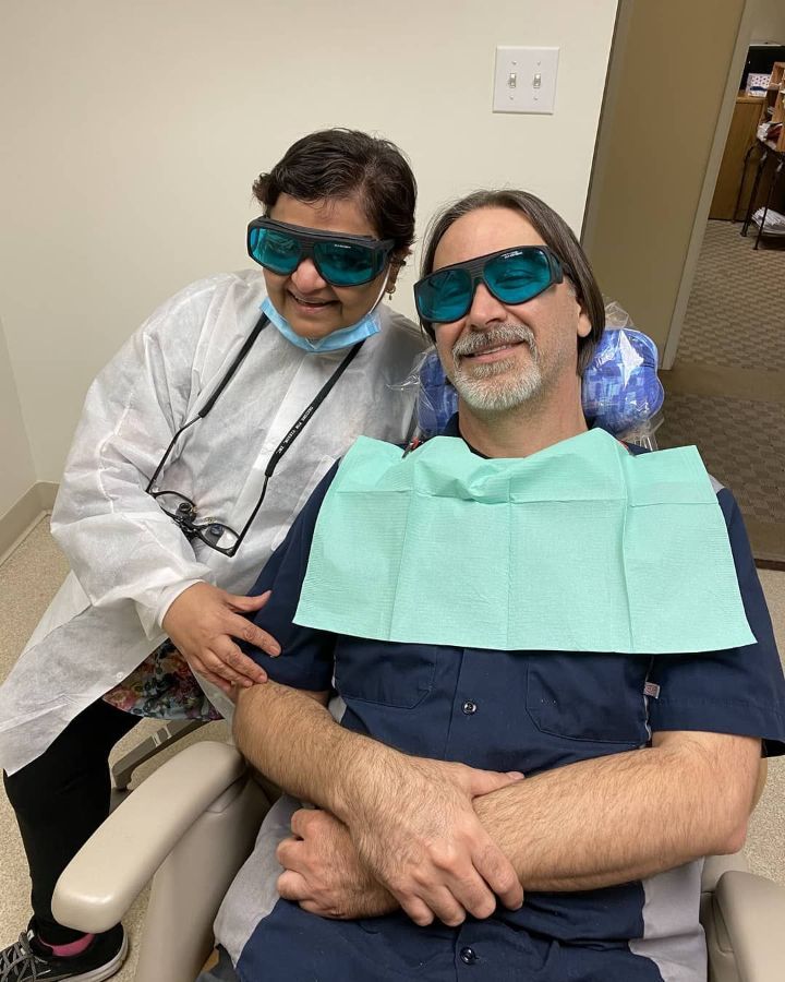 A man is sitting in a dental chair with a woman standing next to him.