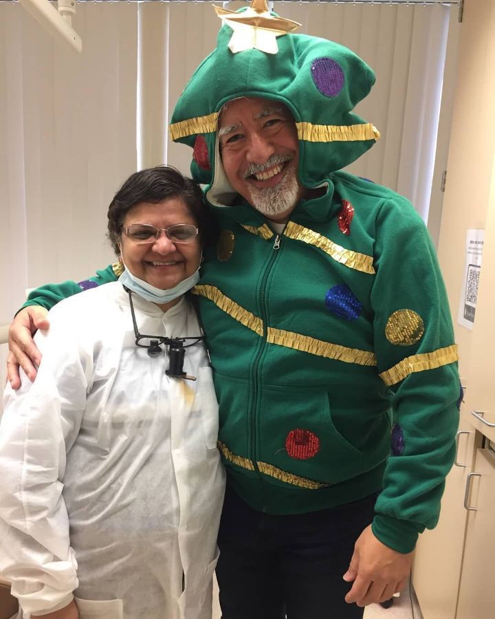 A man in a christmas tree sweater is posing for a picture with a woman in a white coat.