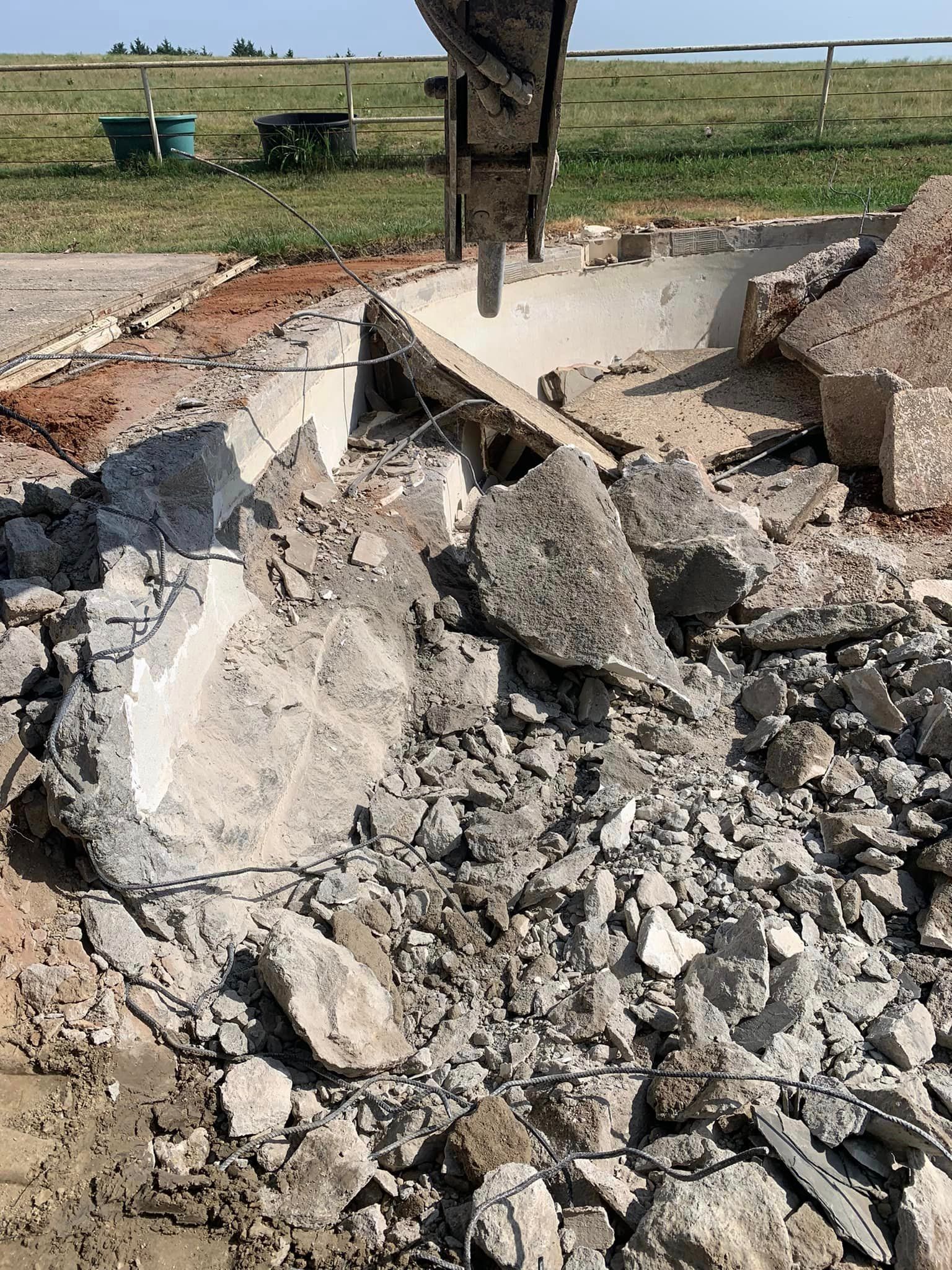 Demolition site, a hydraulic excavator breaking concrete. Debris and destruction fill the frame.
