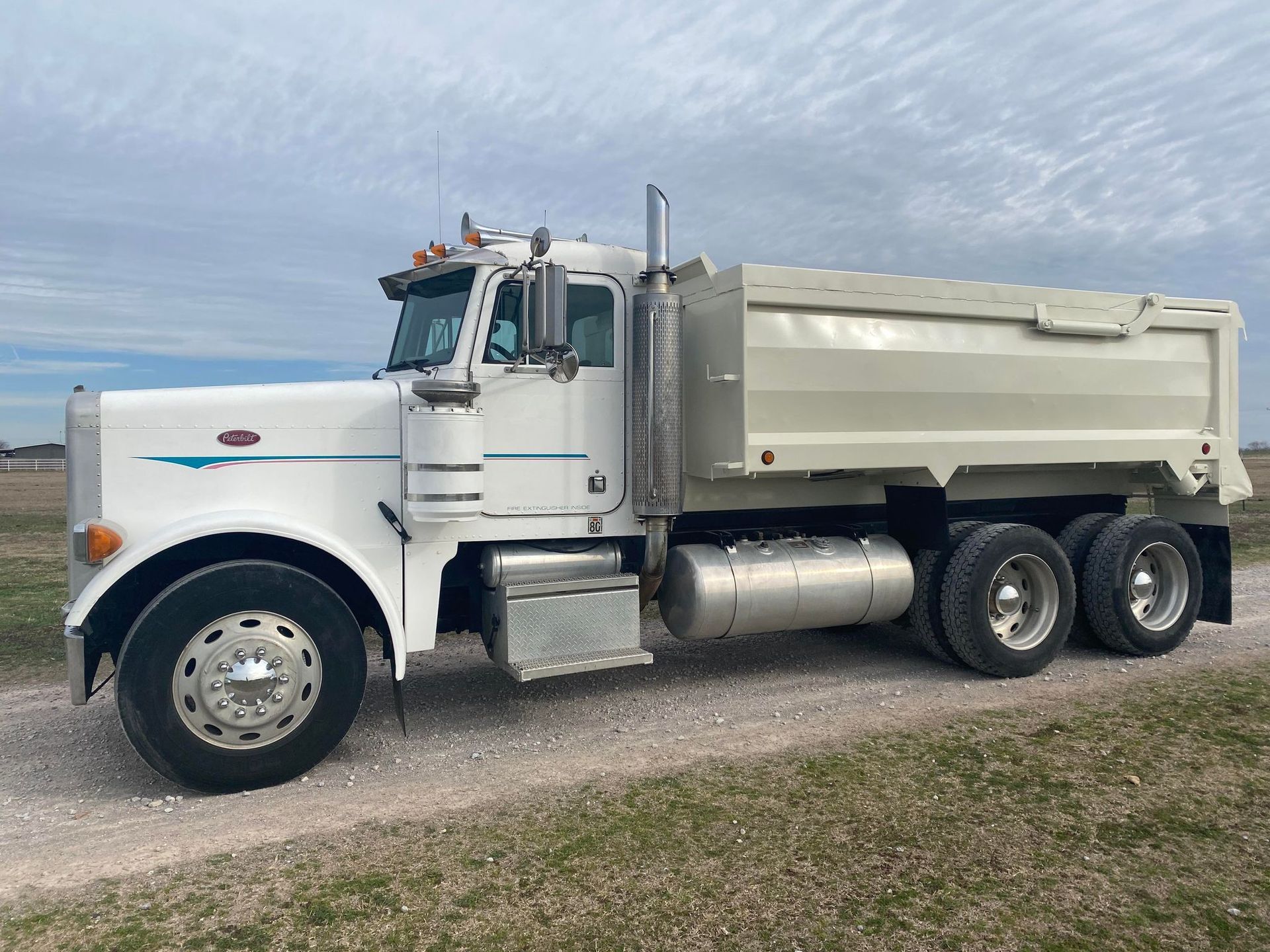 White dump truck on a dirt road in a field under a cloudy sky.