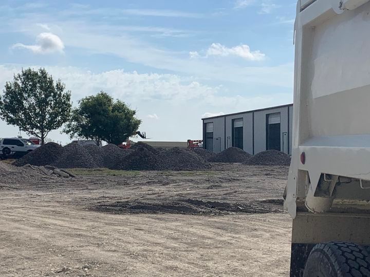Construction site with gravel piles, a white truck, and a building under a cloudy sky.