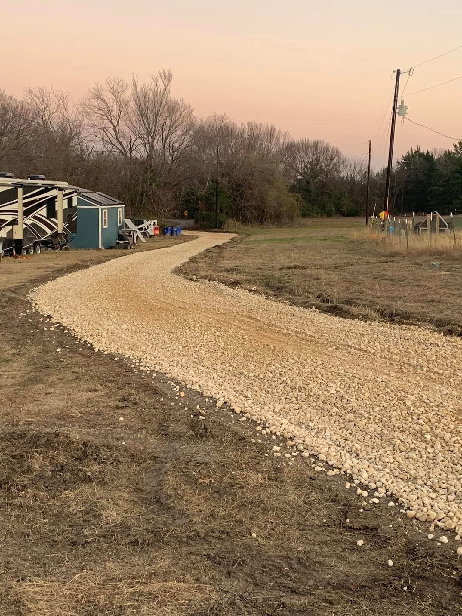 A gravel path winds through a grassy field towards small buildings; dusky sky overhead.