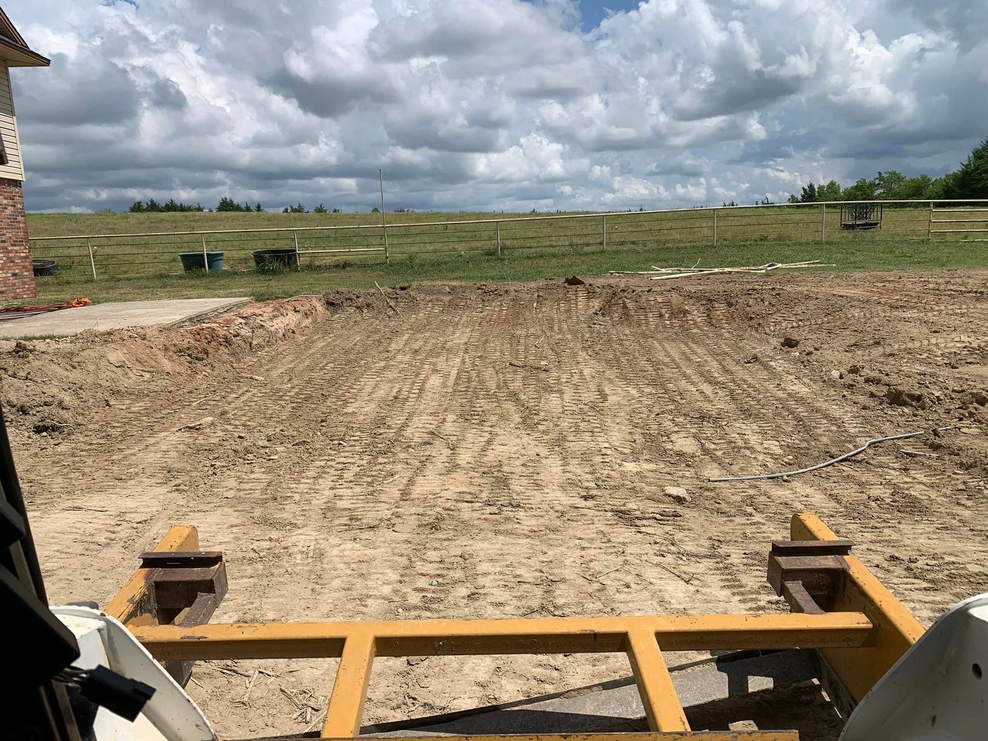Bobcat driving over a dirt field, near a golf course on a cloudy day.