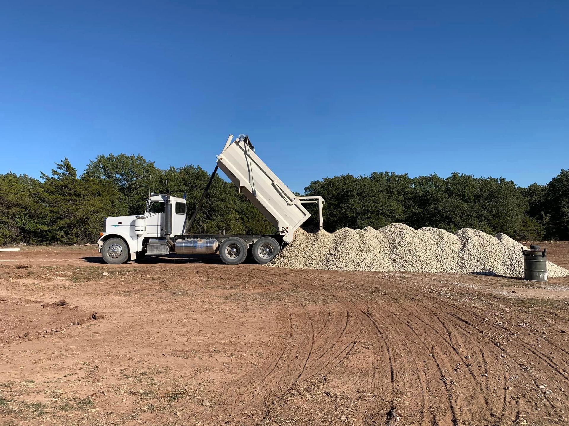 Dump truck dumping gravel on a dirt lot under a blue sky.