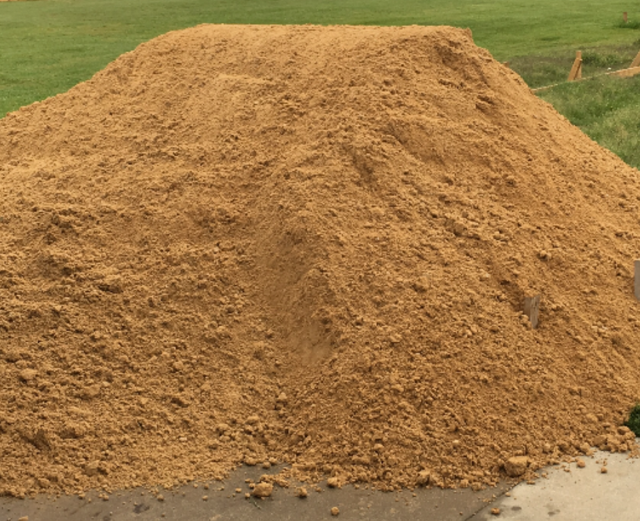 A pile of dirt is sitting on the side of a road next to a house.