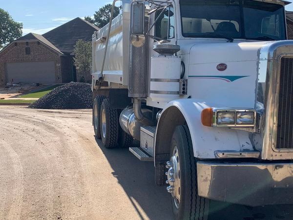 White dump truck parked on a road with a pile of gravel in front of a house.