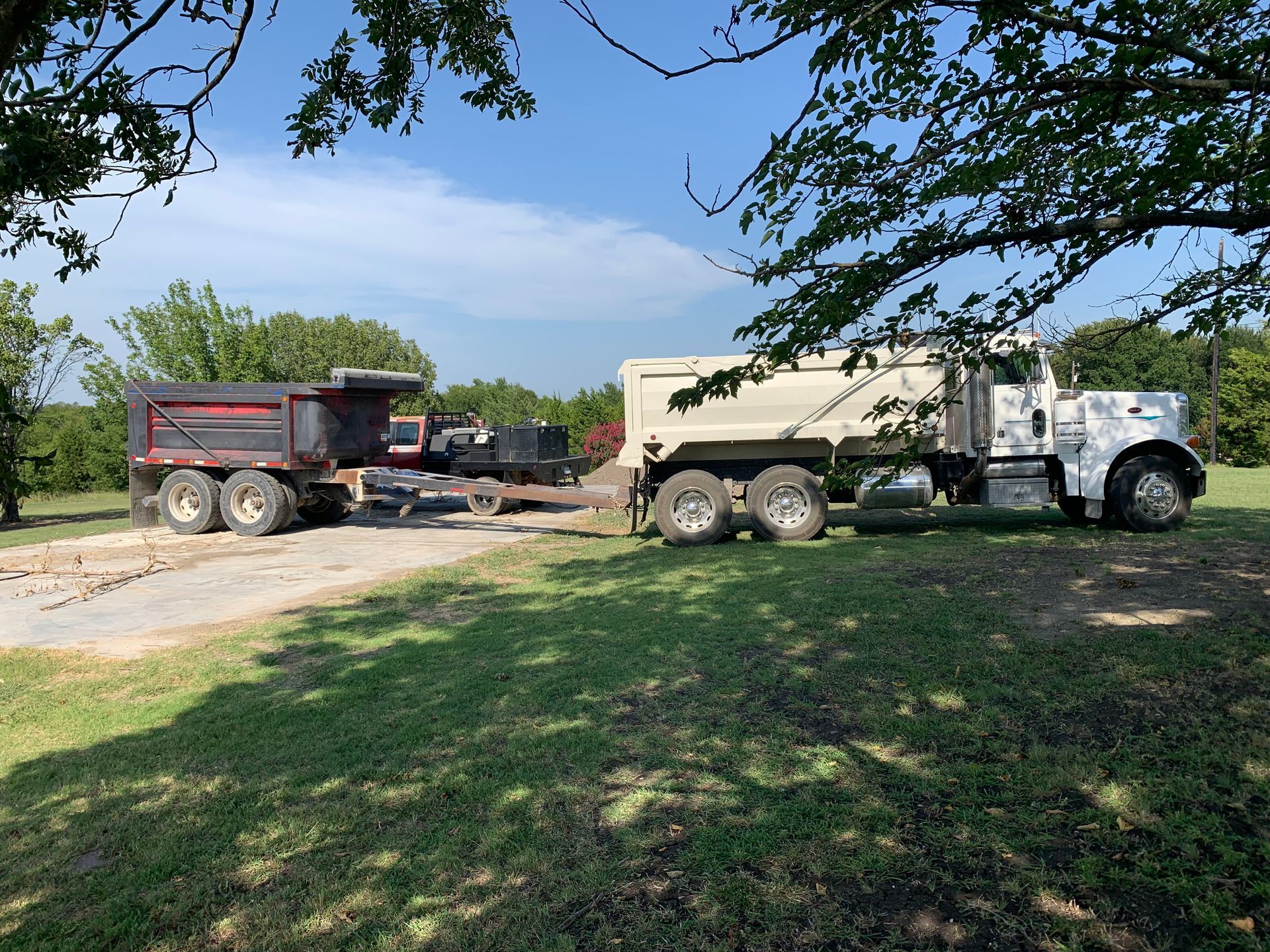A tan semi-truck with a dump trailer on a gravel driveway; sunny day.