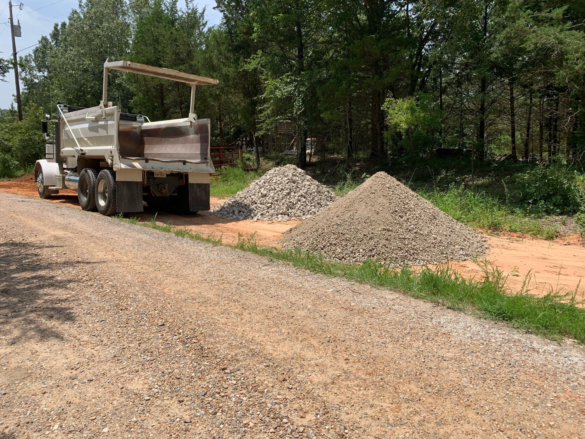 A dump truck unloading gravel onto a dirt road with piles of gravel alongside the road.