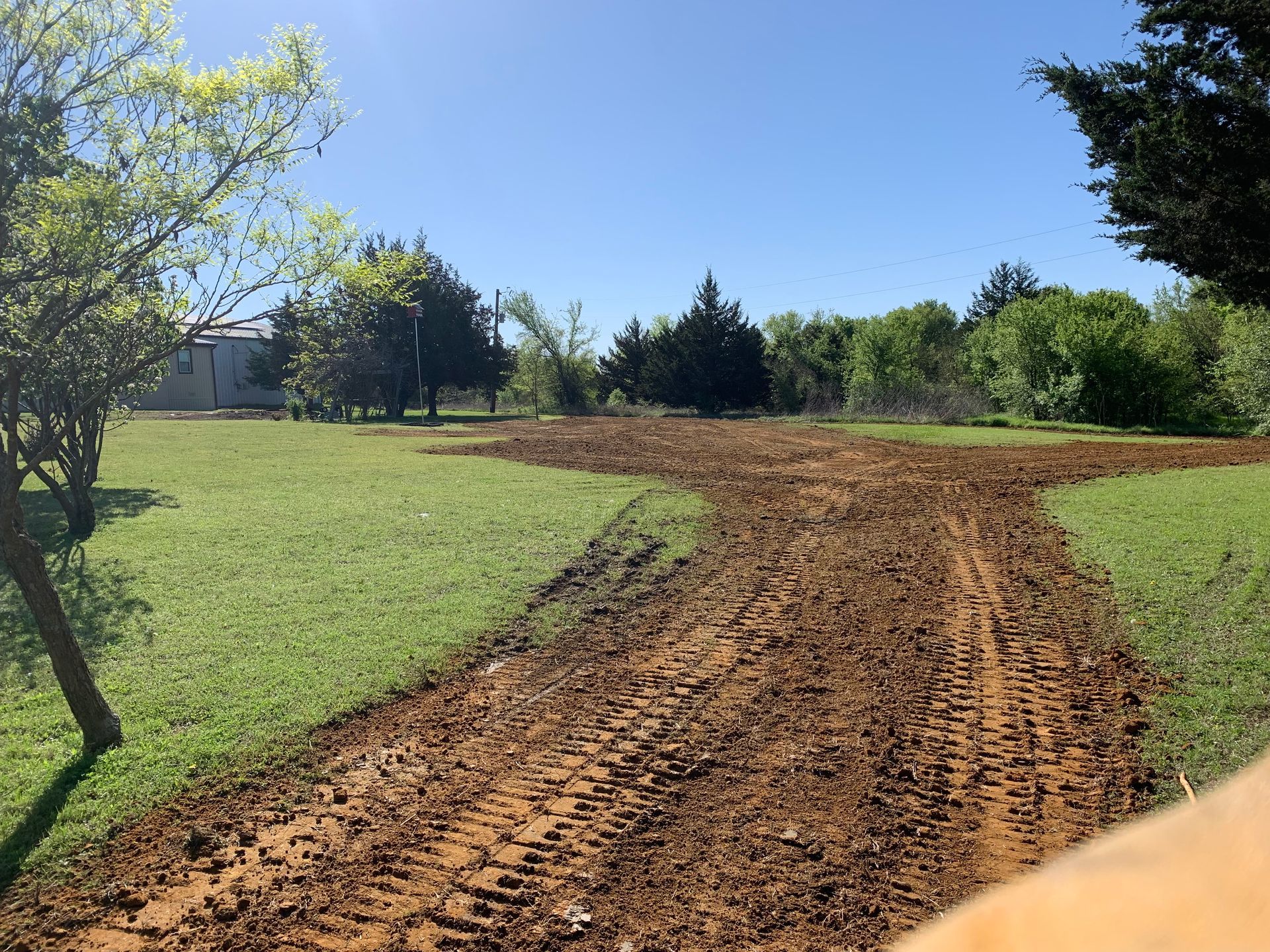 Muddy dirt path with tire tracks across green grass, trees in background.