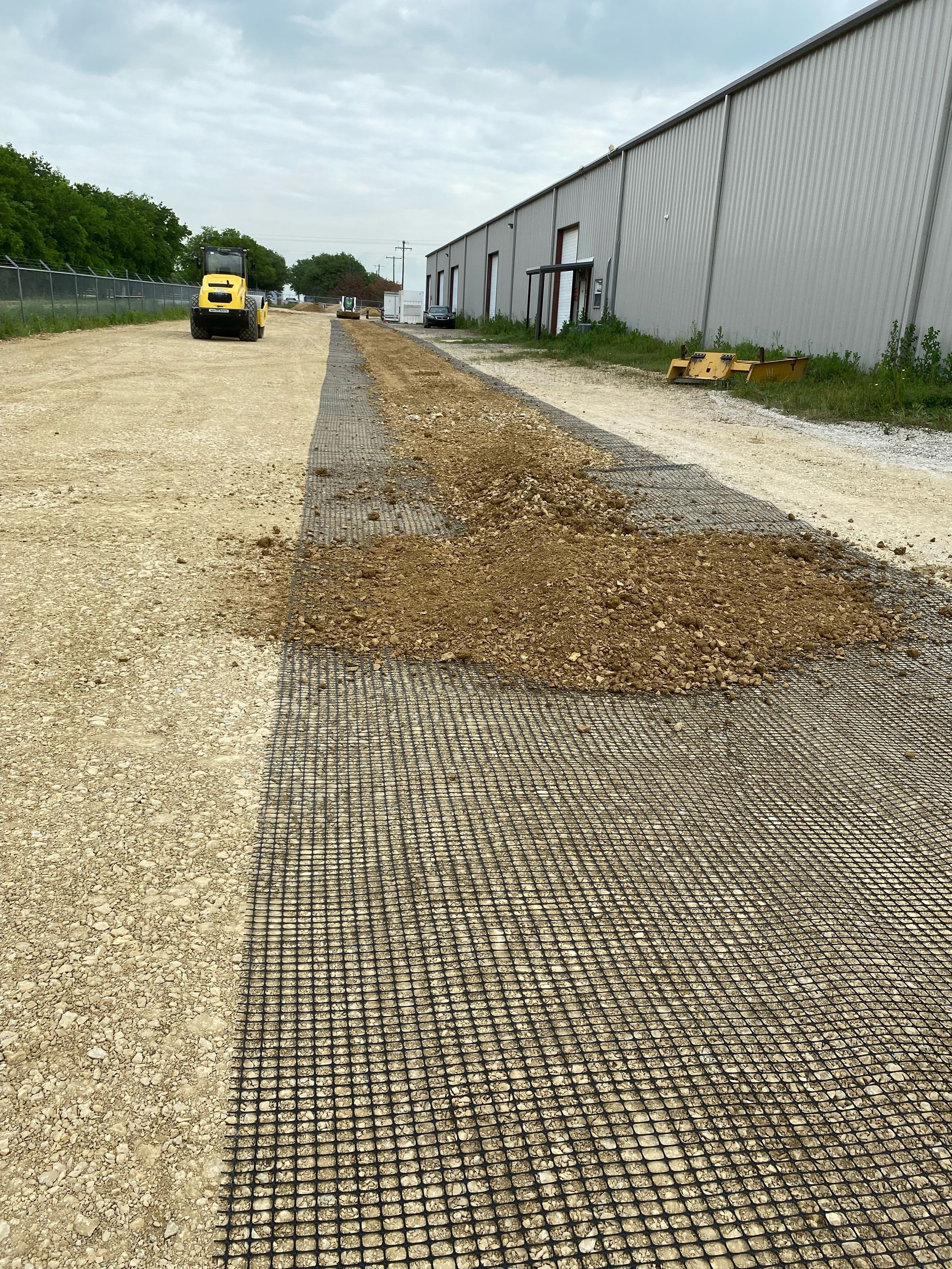 Construction of a gravel path. Black mesh is being covered by gravel. Roller in the background.