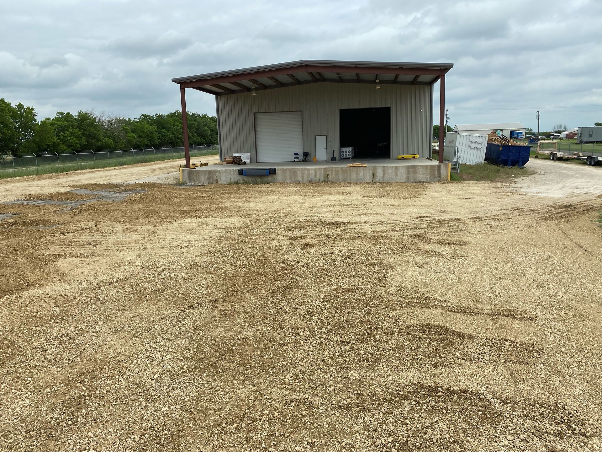 Metal building with loading dock on gravel. Trees in the background under a cloudy sky.