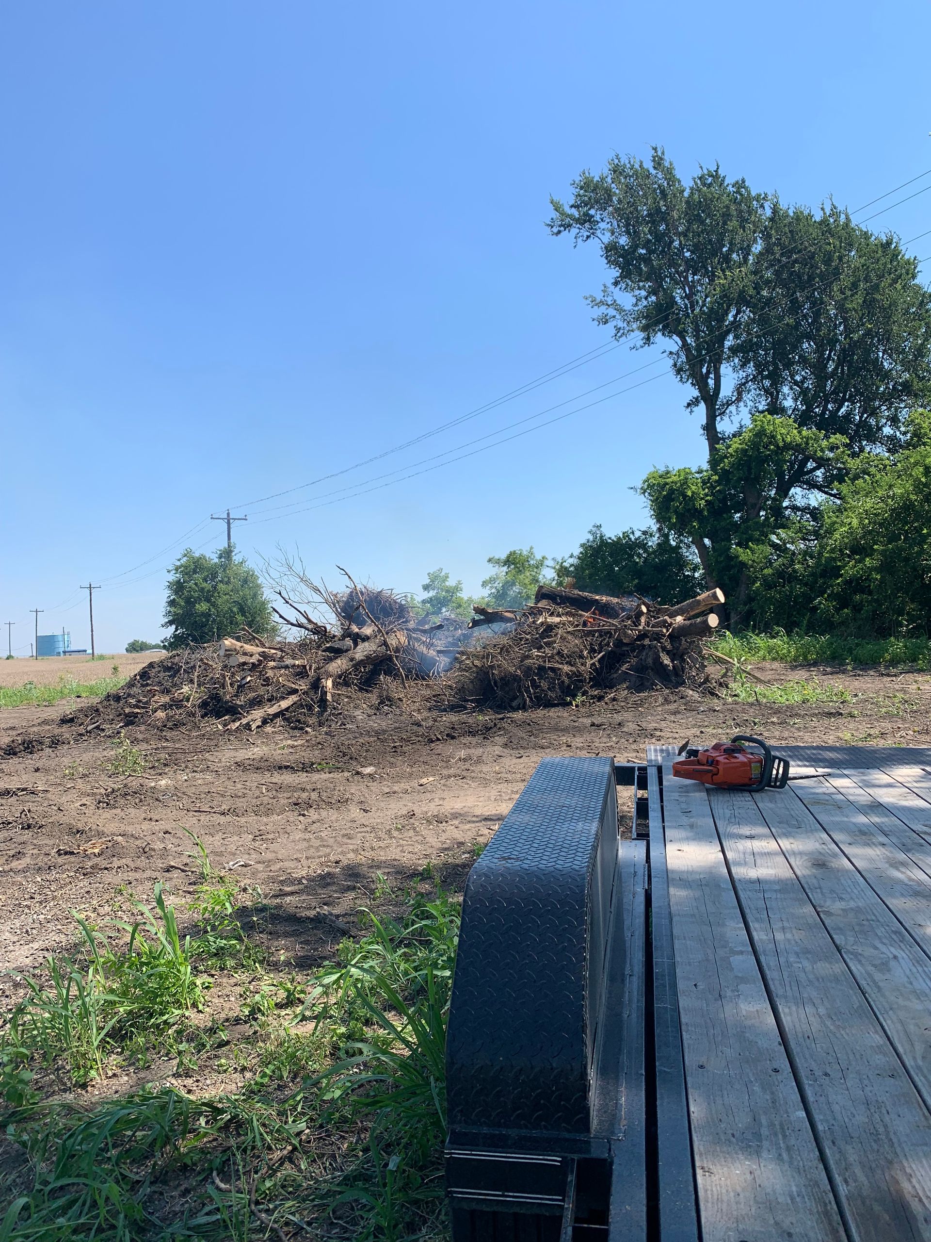Wood debris piles burning near a trailer on a sunny day.