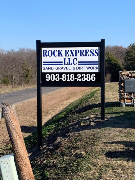 A sign for rock express llc is sitting on the side of a dirt road.