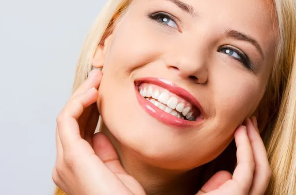 A close up of a woman smiling with her hands on her face.