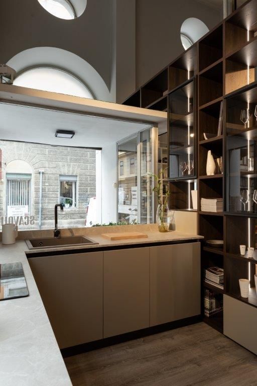 Cucina moderna con mobili in legno scuro, isola centrale e grande finestra ad arco che si affaccia su un cortile.