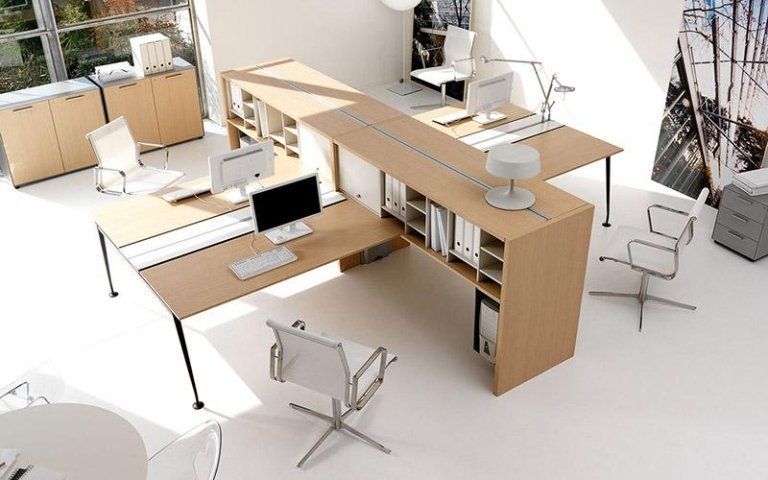 Ufficio moderno open space con scrivanie in legno chiaro, computer e sedie girevoli bianche in uno spazio di lavoro luminoso.