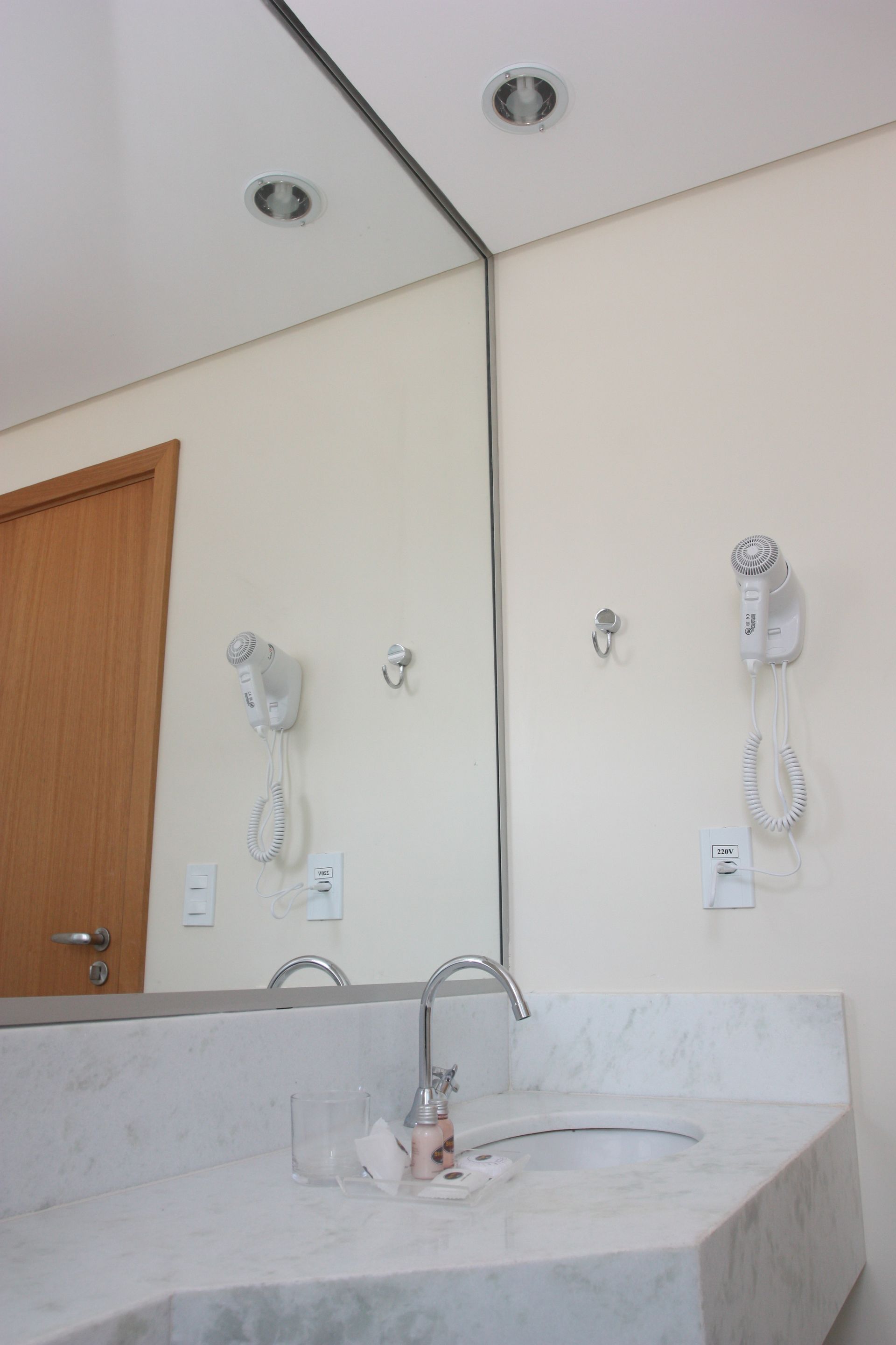 Banheiro com espelho grande, pia de mármore, torneira, secador de cabelo e luminárias.