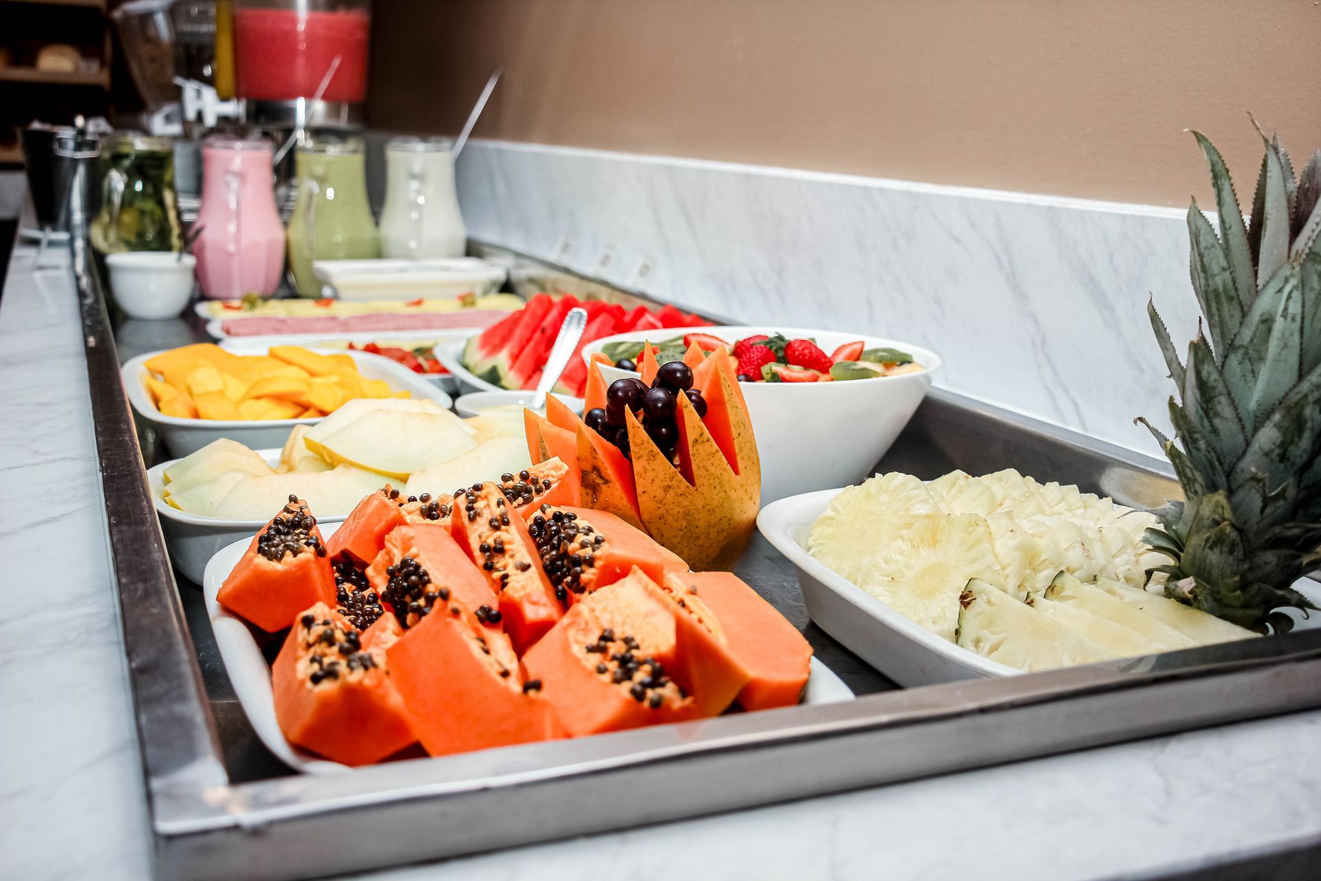 Buffet de frutas com mamão, melancia, manga, abacaxi e sucos diversos.